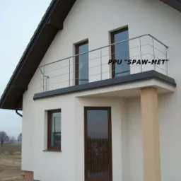 Zewnętrzny widok domu z balkonem zabezpieczonym metalową, spawaną balustradą z rurek, widoczny napis 'PPU SPAW-MET'.