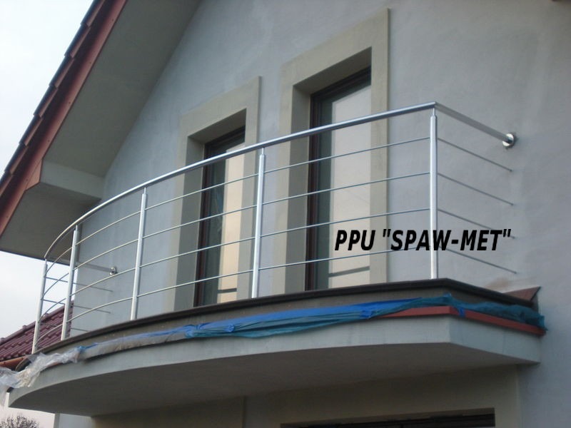 Barierka balkonowa ze stali nierdzewnej, z widocznym zaokrąglonym kształtem i poziomymi prętami, zamontowana na balkonie domu jednorodzinnego z oknami w tle.