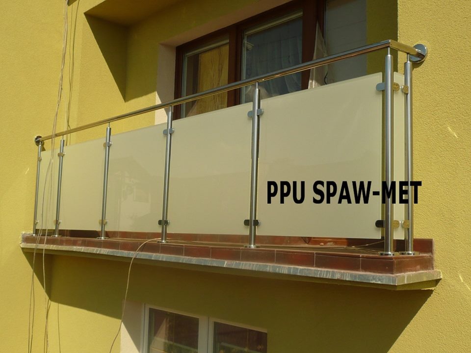 Spawana balustrada balkonowa ze stali nierdzewnej z mlecznym szkłem, zamontowana na żółtej elewacji budynku.