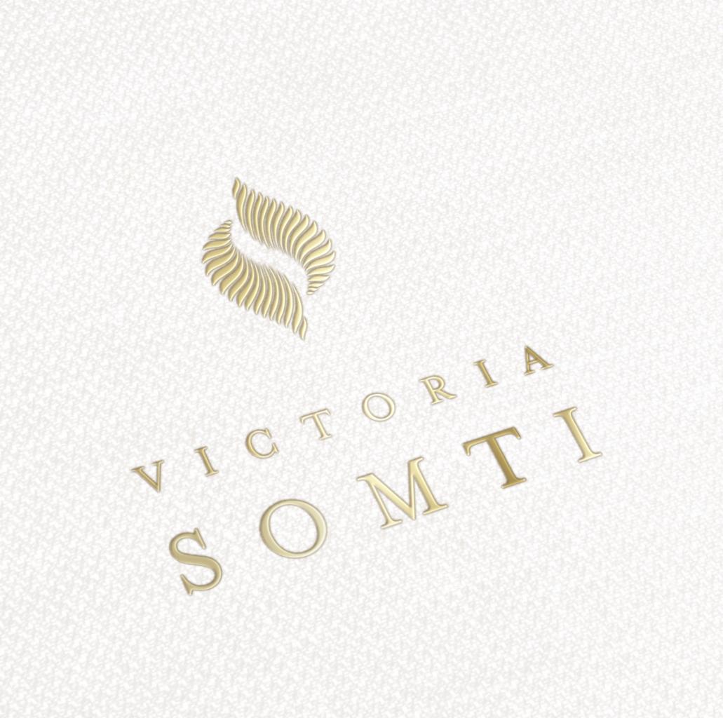 Eleganckie, złote logo 'Victoria Somti' na teksturowanym, kremowym tle z delikatnym wzorem siatki.