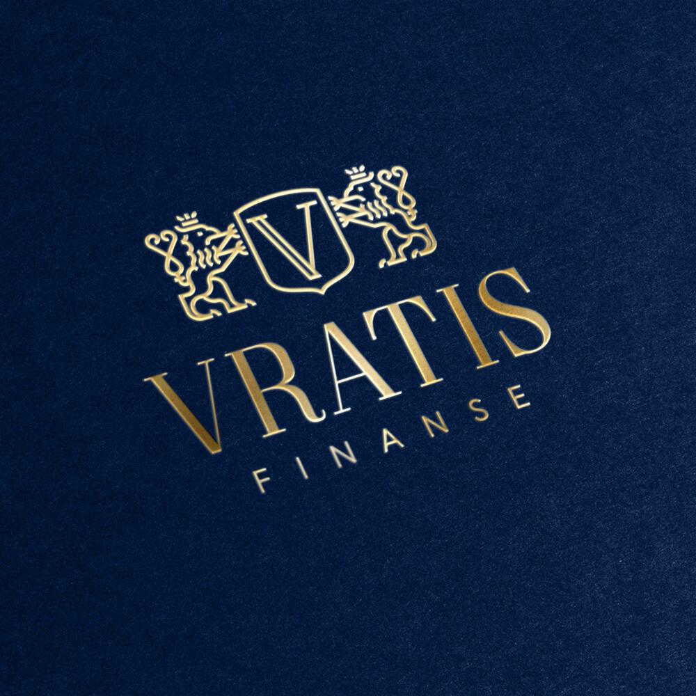 Złote logo 'VRATIS FINANSE' z heraldycznymi lwami i tarczą na granatowym tle z fakturą papieru.