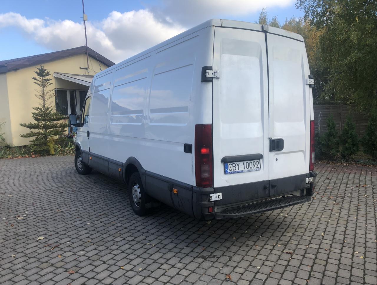 Biały samochód dostawczy Iveco z numerem rejestracyjnym CBY 10092 zaparkowany na brukowanym podjeździe przed budynkiem w słoneczny dzień.