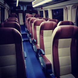 F.H.U. Wolbus - Wnętrze autobusu z rzędami foteli w kolorze bordowo-beżowym, niebieska podłoga, widok z przodu pojazdu, oświetlenie sufitowe.