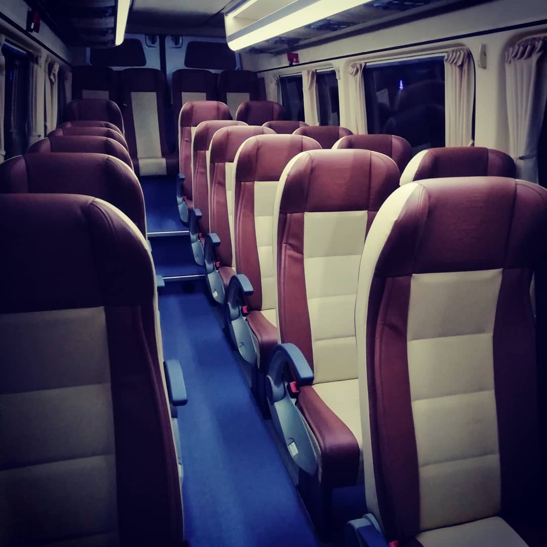 Wnętrze autobusu z rzędami foteli w kolorze bordowo-beżowym, niebieska podłoga, widok z przodu pojazdu, oświetlenie sufitowe.