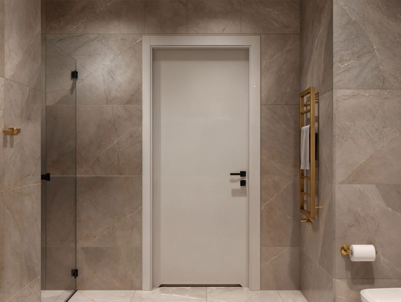 Elegancka łazienka z kabiną prysznicową, grzejnikiem drabinkowym w kolorze złota i płytkami imitującymi marmur. Minimalistyczny wystrój z akcentami złota.