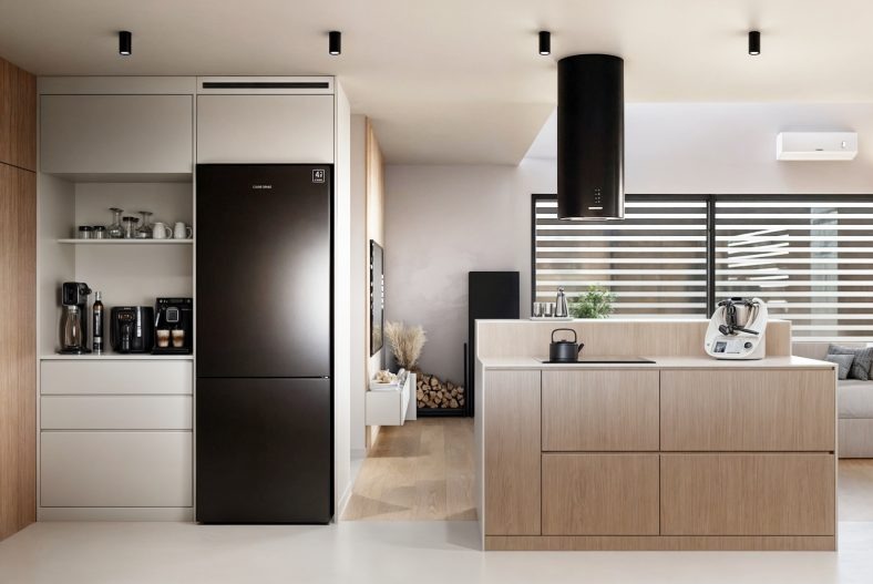 Nowoczesna kuchnia w jasnych barwach z czarną lodówką i okapem. Minimalistyczny design, drewniane wykończenia, oświetlenie punktowe i duża powierzchnia blatu roboczego.