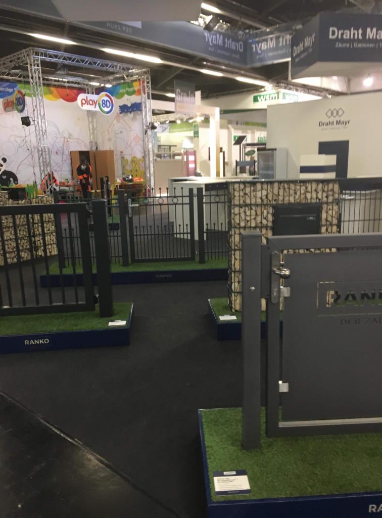 Ekspozycja różnych modeli ogrodzeń i bram firmy Ranko na targach, z widocznymi elementami z gabionów i sztucznej trawy, w tle stoisko Play 8D.
