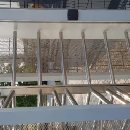 Nowoczesny kołowrót bramowy z czytnikiem kart i kamerą monitoringu, widok z dołu na stalowe pręty i perforowaną blachę.