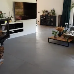 Jasnoszara, bezspoinowa podłoga w przestronnym salonie z nowoczesnym kominkiem narożnym i minimalistycznym wystrojem.