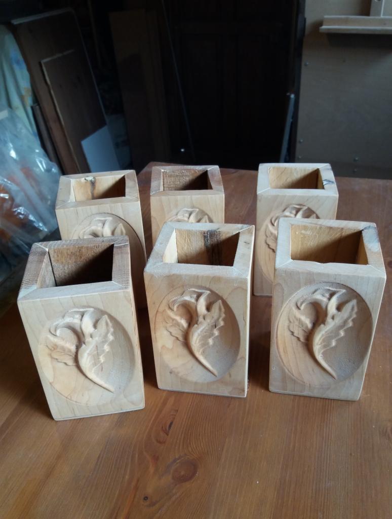 Sześć drewnianych, surowych pojemników z wyżłobionym motywem roślinnym, ustawionych na drewnianym blacie.