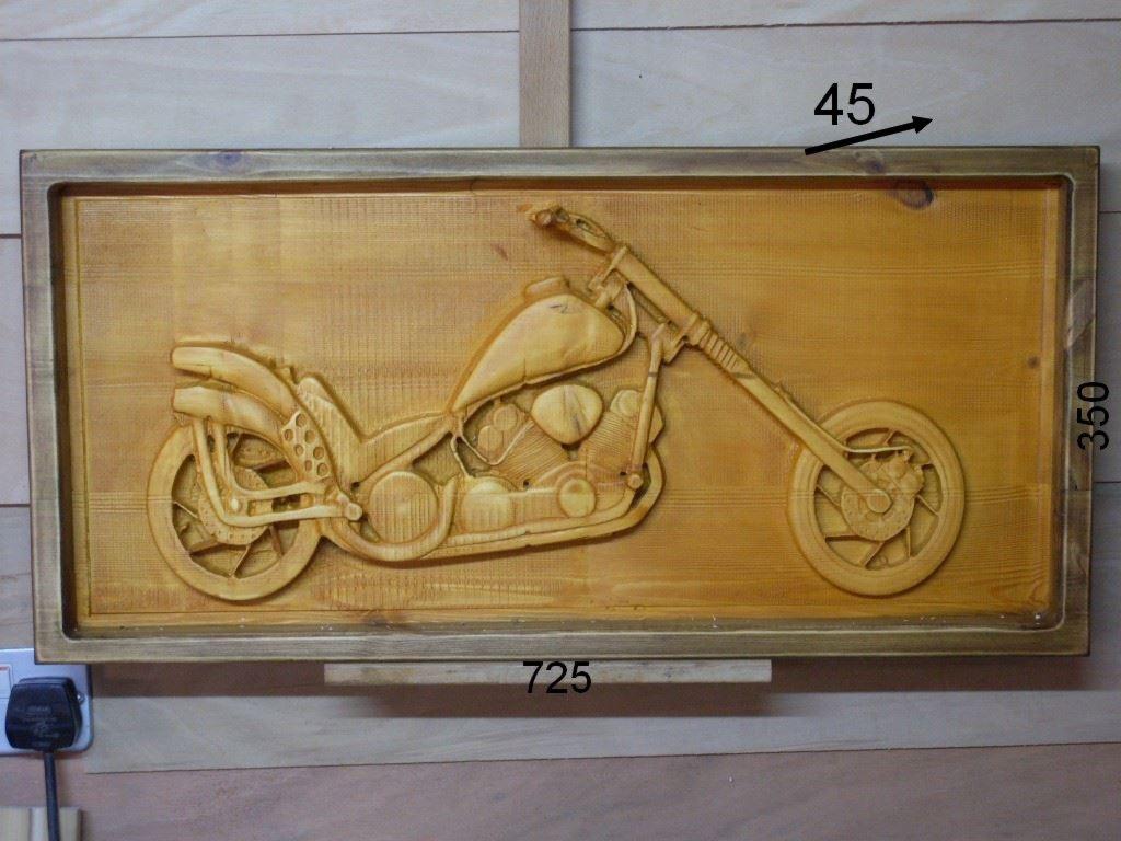 Ręcznie rzeźbiony w drewnie obraz motocykla chopper w ramie, widoczne detale silnika i opon, ciepłe oświetlenie podkreśla fakturę drewna.