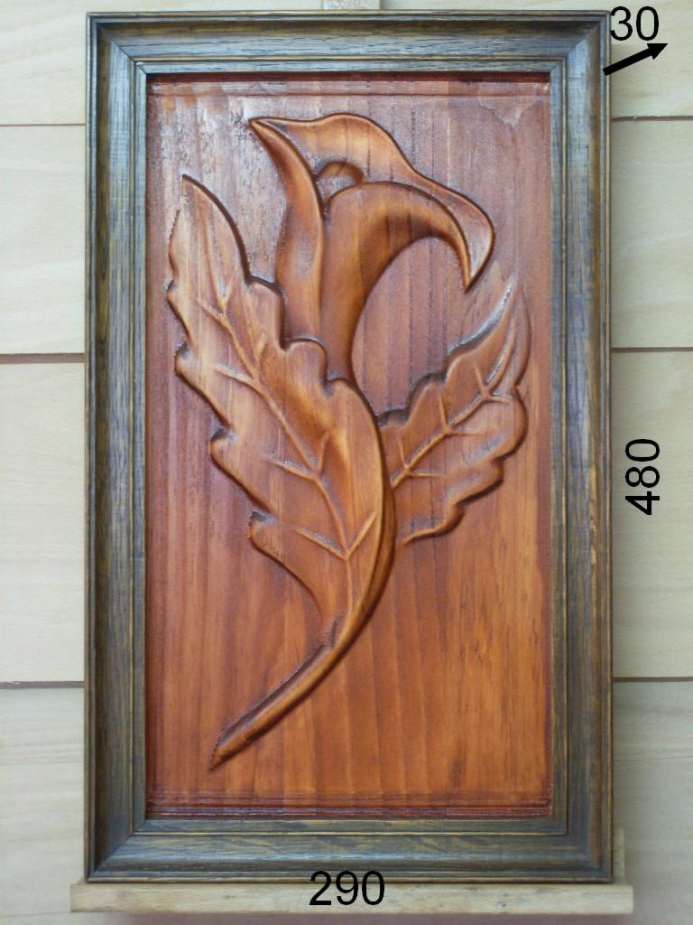 Drewniana płaskorzeźba przedstawiająca stylizowany kwiat kalii i liście, umieszczona w ciemnej, ozdobnej ramie.