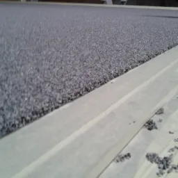 Szara, chropowata powierzchnia, prawdopodobnie dach, z widocznymi elementami konstrukcyjnymi i taśmą maskującą zabezpieczającą obszar przed zabrudzeniem.