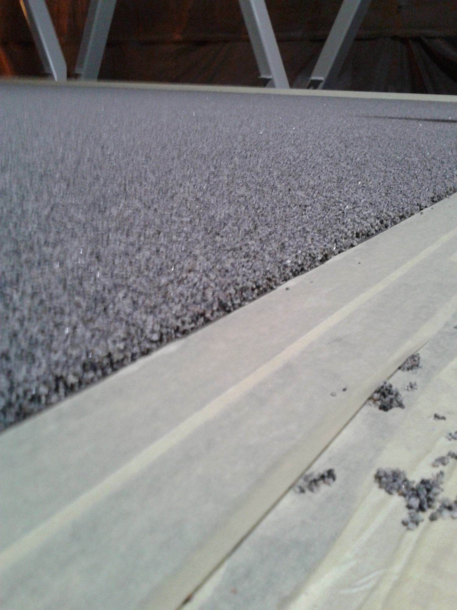 Szara, chropowata powierzchnia, prawdopodobnie dach, z widocznymi elementami konstrukcyjnymi i taśmą maskującą zabezpieczającą obszar przed zabrudzeniem.