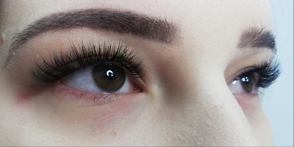 Zbliżenie na oko z brązową tęczówką i przedłużonymi, gęstymi, czarnymi rzęsami. Widoczny delikatny makijaż brwi.
