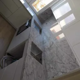 Szara, marmurkowa powierzchnia blatu kuchennego z wbudowanym zlewem, widok z dołu, oświetlona naturalnym światłem z okna dachowego.