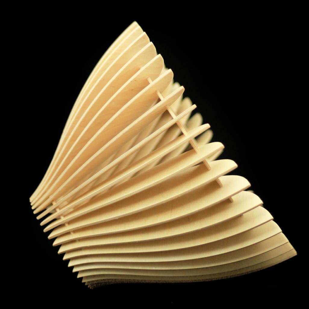 Abstrakcyjna drewniana rzeźba z warstw giętej sklejki, połączonych poprzecznymi listewkami, na czarnym tle.