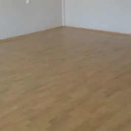 Jasna, dębowa podłoga parkietowa ułożona w pustym pokoju z białymi ścianami i widocznymi gniazdkami elektrycznymi.