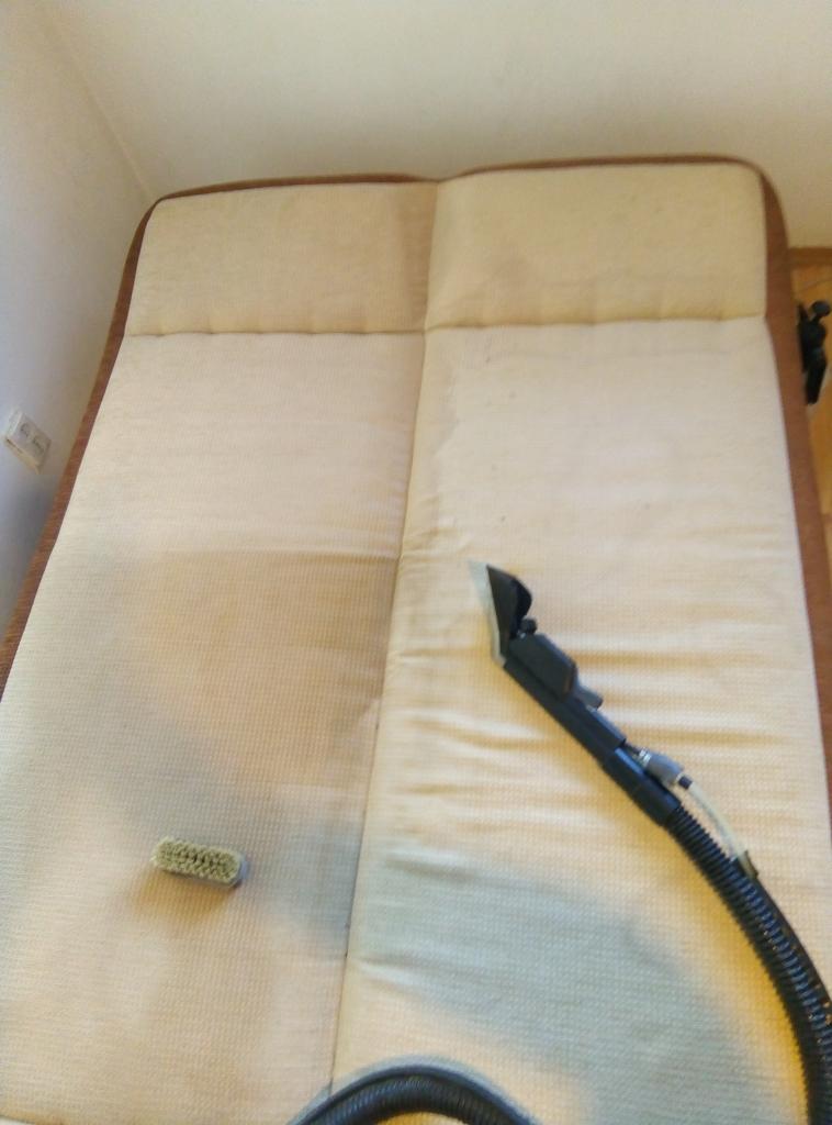 Beżowa kanapa z widoczną różnicą po czyszczeniu - jedna część jest wyraźnie jaśniejsza po użyciu odkurzacza piorącego, obok leży szczotka.