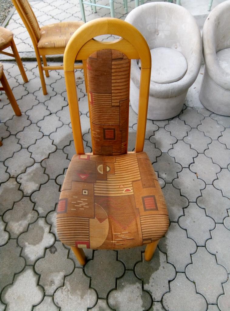 Krzesło z drewnianą ramą i tapicerką w geometryczne wzory, ustawione na betonowej kostce, w tle inne krzesła i fotele.