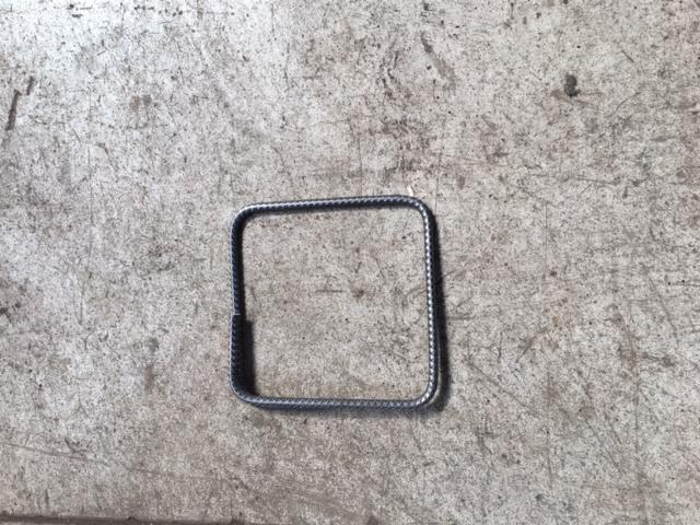 Kwadratowy element gięty z pręta żebrowanego leżący na szarej, betonowej powierzchni.