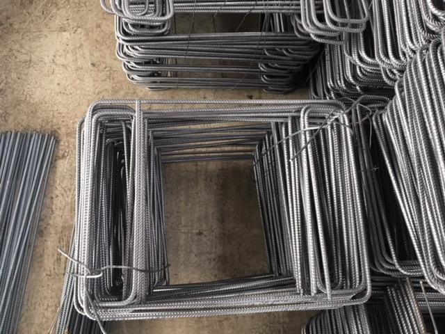 Stosy kwadratowych i prostokątnych elementów zbrojeniowych, widoczne ślady magazynowania na podłożu.