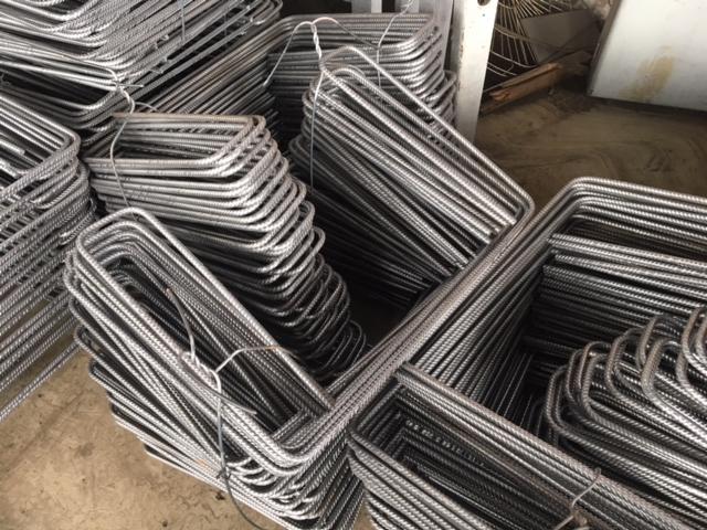 Stosy wygiętych prętów zbrojeniowych, ułożone na betonowej posadzce w magazynie, widoczne ślady rdzy.