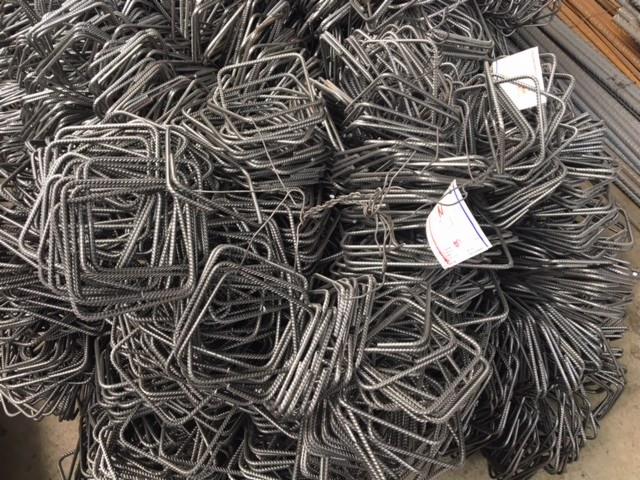 Stos kwadratowych, stalowych strzemion z żebrowanej stali, związanych drutem, z widoczną etykietą.