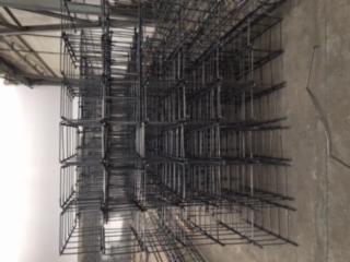 Siatka z prętów zbrojeniowych ułożona w stos na betonowej posadzce, widoczne spawane łączenia.