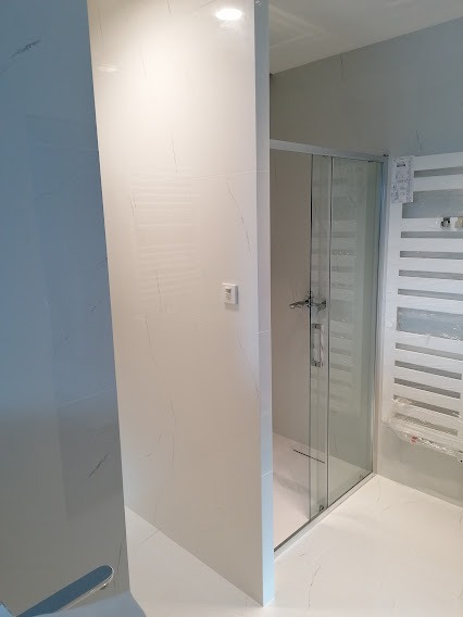 Nowoczesna łazienka z kabiną prysznicową typu walk-in, wykończona białymi płytkami z delikatnym szarym żyłkowaniem, grzejnik drabinkowy na ścianie.