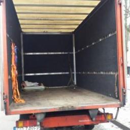 Przeprowadzka.org - Pusta przestrzeń ładunkowa samochodu dostawczego z otwartymi drzwiami, widoczne pasy transportowe i mały pakunek, zimowa sceneria w tle.