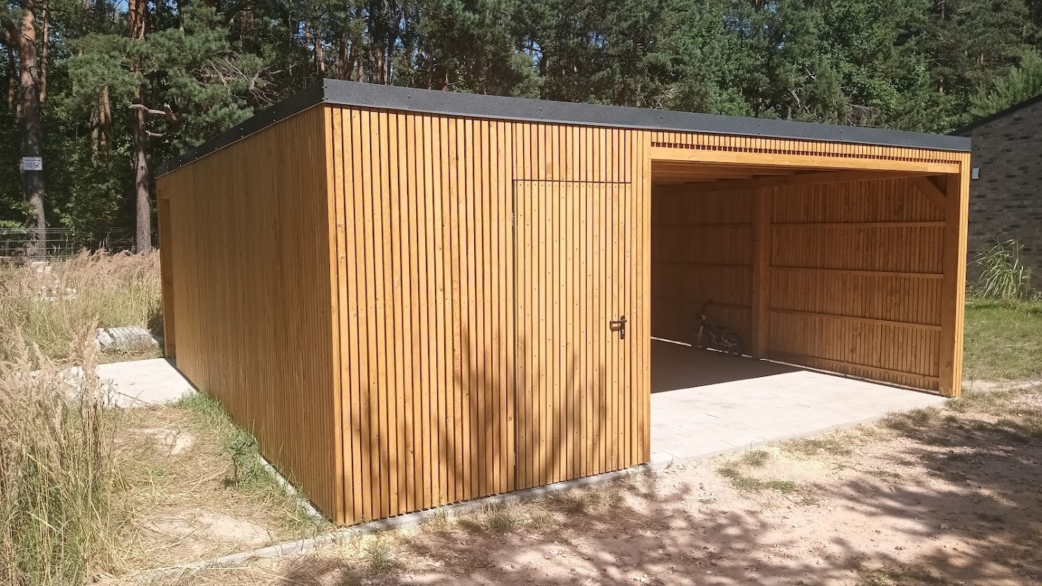 Nowoczesna, drewniana altana z zamykanym pomieszczeniem gospodarczym, wykończona pionowymi listwami, na tle zieleni i drzew.