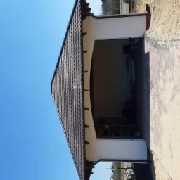 Nowoczesny dom z ciemnobrązowym dachem krytym dachówką karpiówką, widok na garaż z otwartą bramą i częściowo wykończonym terenem wokół.