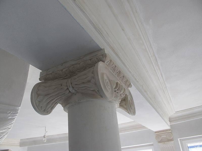 Detal kolumny z kapitelem jońskim w trakcie prac wykończeniowych, surowy tynk na kolumnie i listwach sufitowych, widoczne ślady szpachlowania.