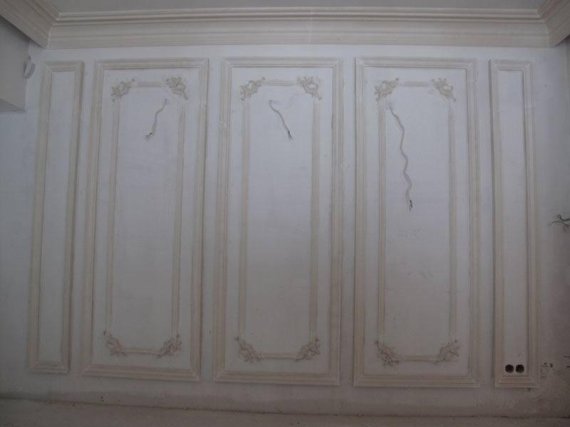 Ściana z dekoracyjnymi panelami i sztukaterią w trakcie prac wykończeniowych w Zielonce, widoczne niedoskonałości powierzchni przed malowaniem.