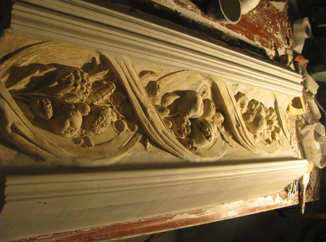 Dekoracyjny gzyms z motywami owoców i roślin, wykonany z gipsu lub stiuku, w trakcie renowacji, widoczne narzędzia i ślady pracy.