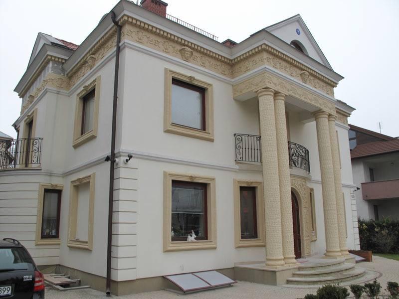 Elewacja domu jednorodzinnego z dekoracyjnymi kolumnami i sztukaterią w odcieniach bieli i beżu, widok z zewnątrz, samochód osobowy zaparkowany z boku budynku.