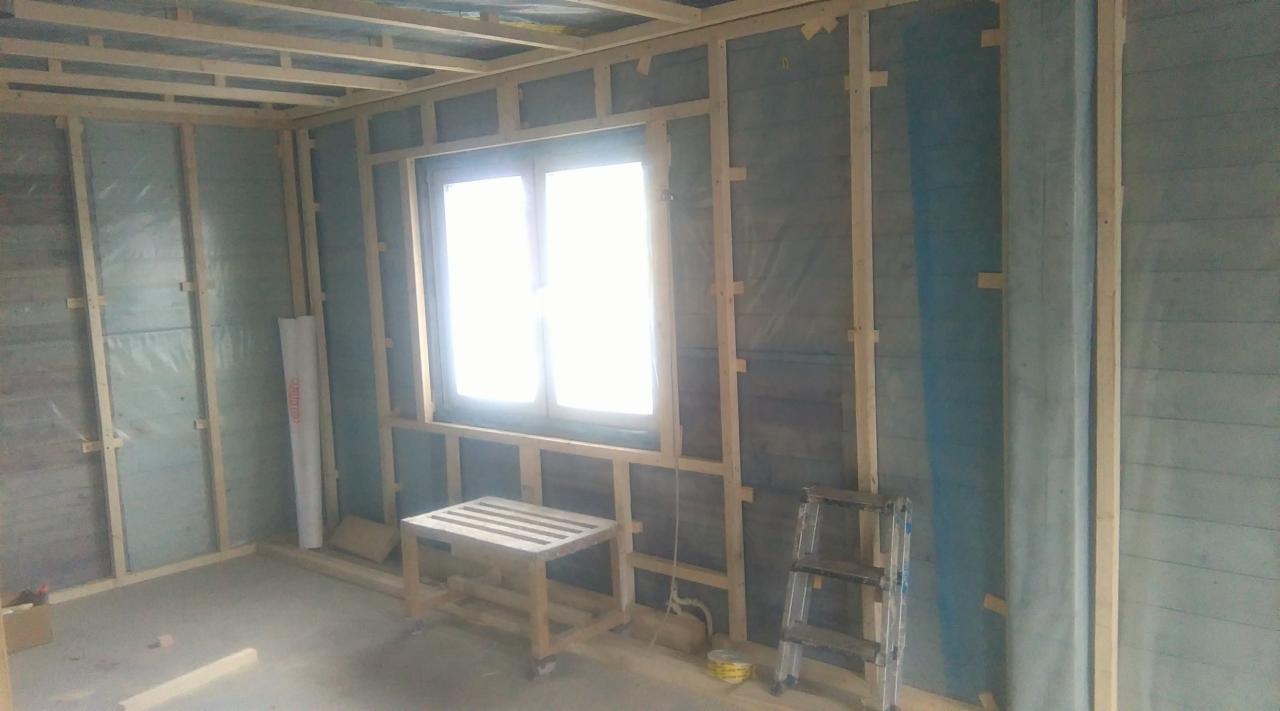 Wnętrze w trakcie remontu: drewniana konstrukcja ścian z oknem, izolacja folią paroizolacyjną, drabina aluminiowa, niski stolik z desek.