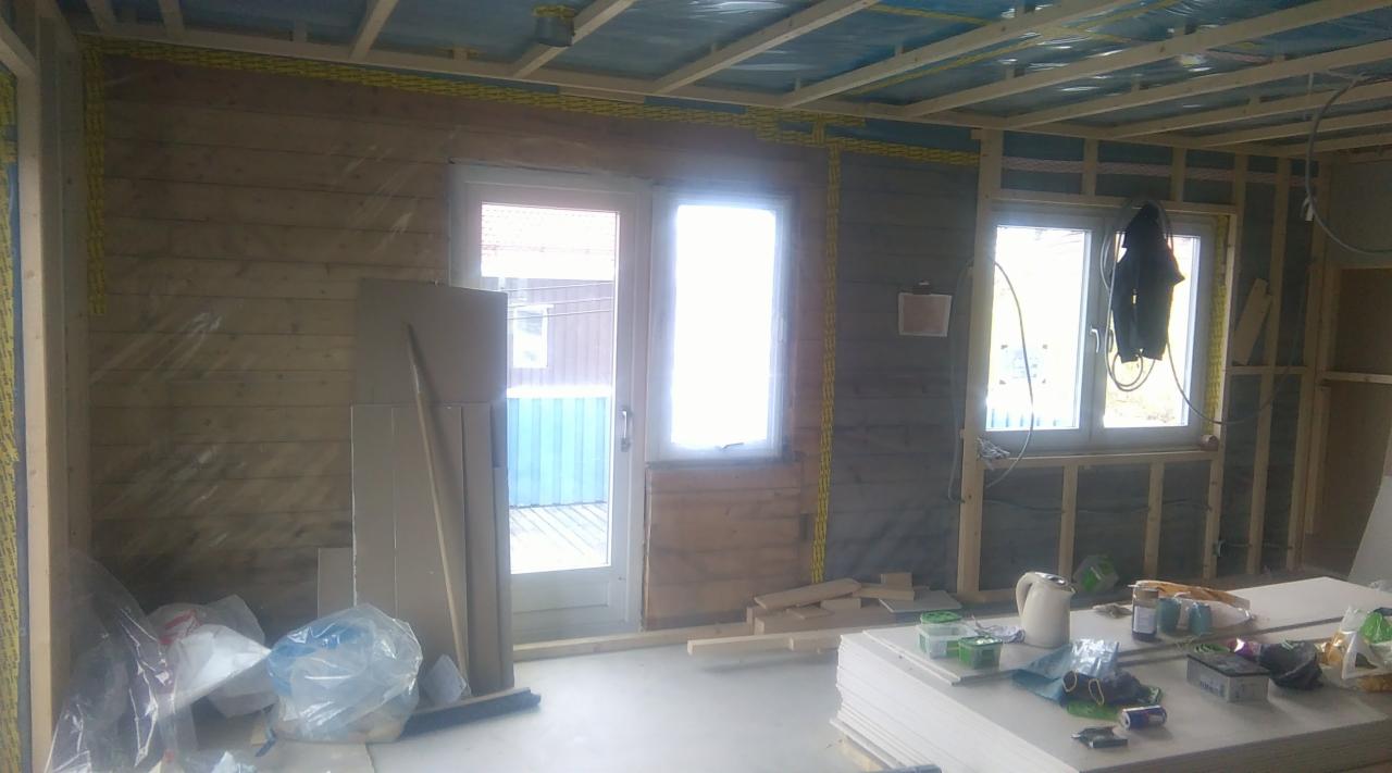 Wnętrze w trakcie prac wykończeniowych: drewniana boazeria na ścianach, widoczne profile konstrukcyjne, okna i drzwi zamontowane, żółte kable elektryczne w peszlach, płyty gipsowo-kartonowe...