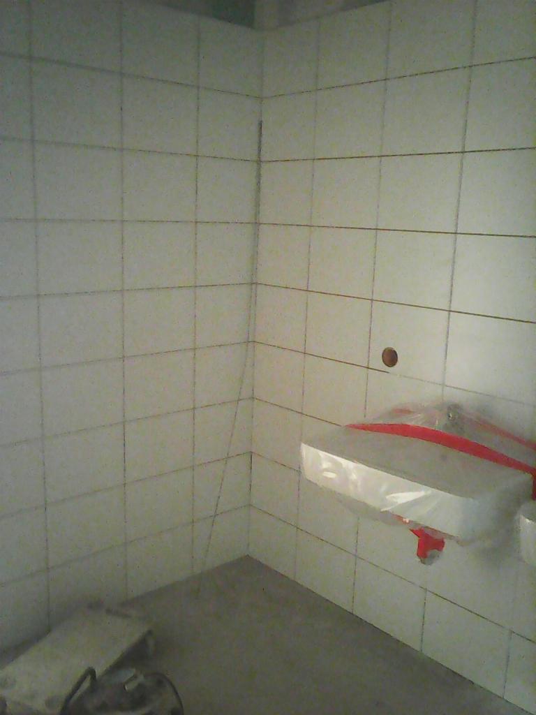 Świeżo wykafelkowana ściana i podłoga w łazience w Berlinie, z zabezpieczoną folią umywalką, ukazująca etap prac wykończeniowych.