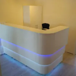 Biała, lakierowana lada recepcyjna z podświetleniem LED na tle jasnych ścian i podłogi z płytek.