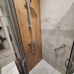 EXPERT - Nowoczesna kabina prysznicowa z chromowaną armaturą, brązowymi i marmurkowymi płytkami oraz uchwytem dla osób z niepełnosprawnościami.