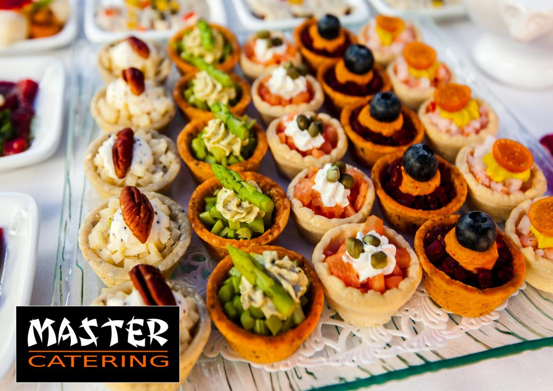 Różnorodne tartaletki na przezroczystym szklanym talerzu, wypełnione kremem, warzywami i owocami, z logo firmy cateringowej w lewym dolnym rogu.