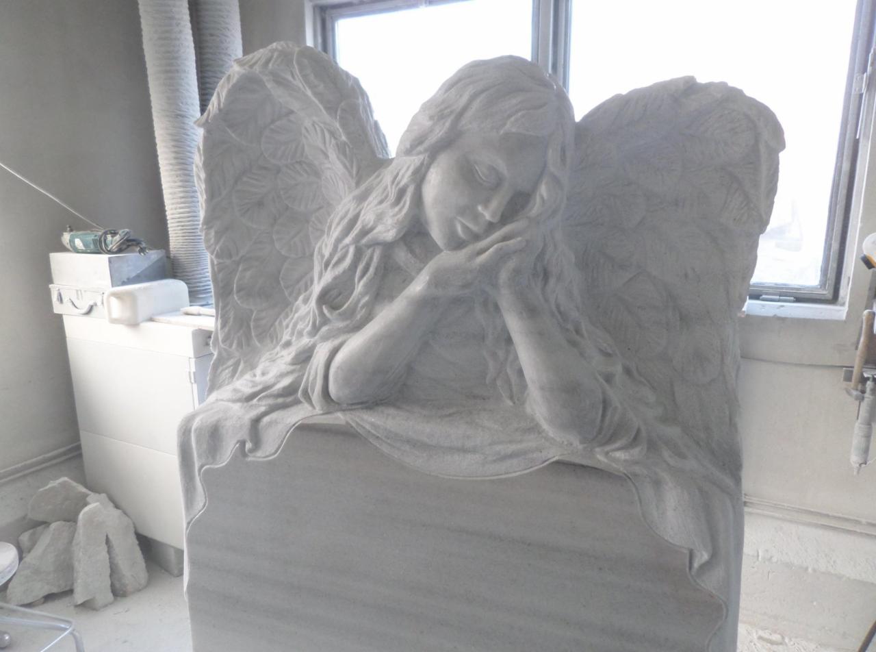 Rzeźba anioła z marmuru, w trakcie tworzenia, widoczne narzędzia kamieniarskie w tle.