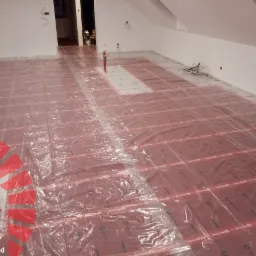 Rozłożone maty grzewcze na podczerwień, pokryte folią ochronną, przygotowane do dalszych prac wykończeniowych w pomieszczeniu na poddaszu.