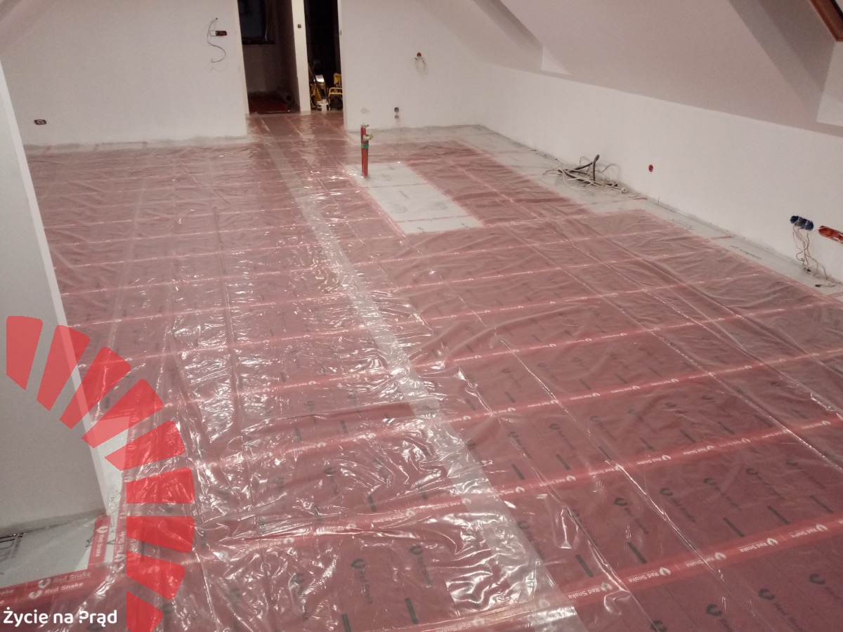 Rozłożone maty grzewcze na podczerwień, pokryte folią ochronną, przygotowane do dalszych prac wykończeniowych w pomieszczeniu na poddaszu.