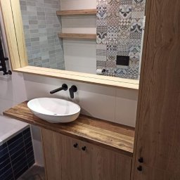 Mateusz Trepczyk Stol-Trep - Łazienka z umywalką nablatową na drewnianym blacie i szafką, drewniane półki i lustro z drewnianą ramą, ściana wyłożona płytkami w geometryczne wzory.