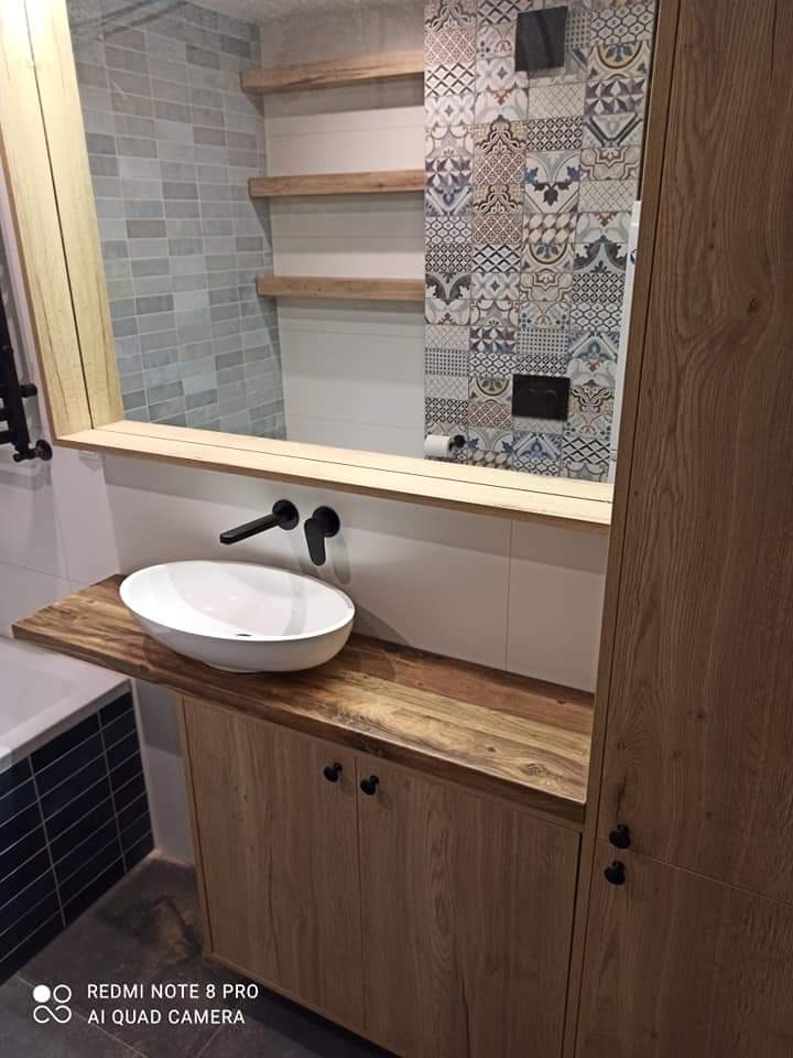 Łazienka z umywalką nablatową na drewnianym blacie i szafką, drewniane półki i lustro z drewnianą ramą, ściana wyłożona płytkami w geometryczne wzory.