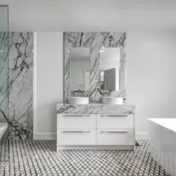 Nowoczesna łazienka z marmurowymi akcentami: ściana prysznicowa, obudowa lustra i blat umywalki z białego marmuru, białe szafki pod umywalkami, wolnostojąca wanna i mozaika na podłodze.