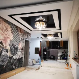 Nowoczesny salon w trakcie wykańczania: dekoracyjna tapeta w kwiaty, lustrzane ściany i podwieszany sufit z czarnym lustrem i żyrandolem.